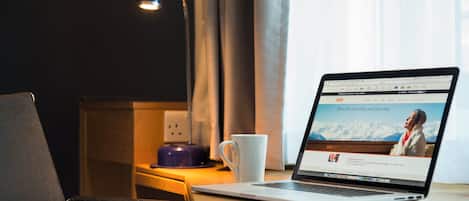 A laptop on a wooden desk with a white mug, a lamp, and a power outlet.