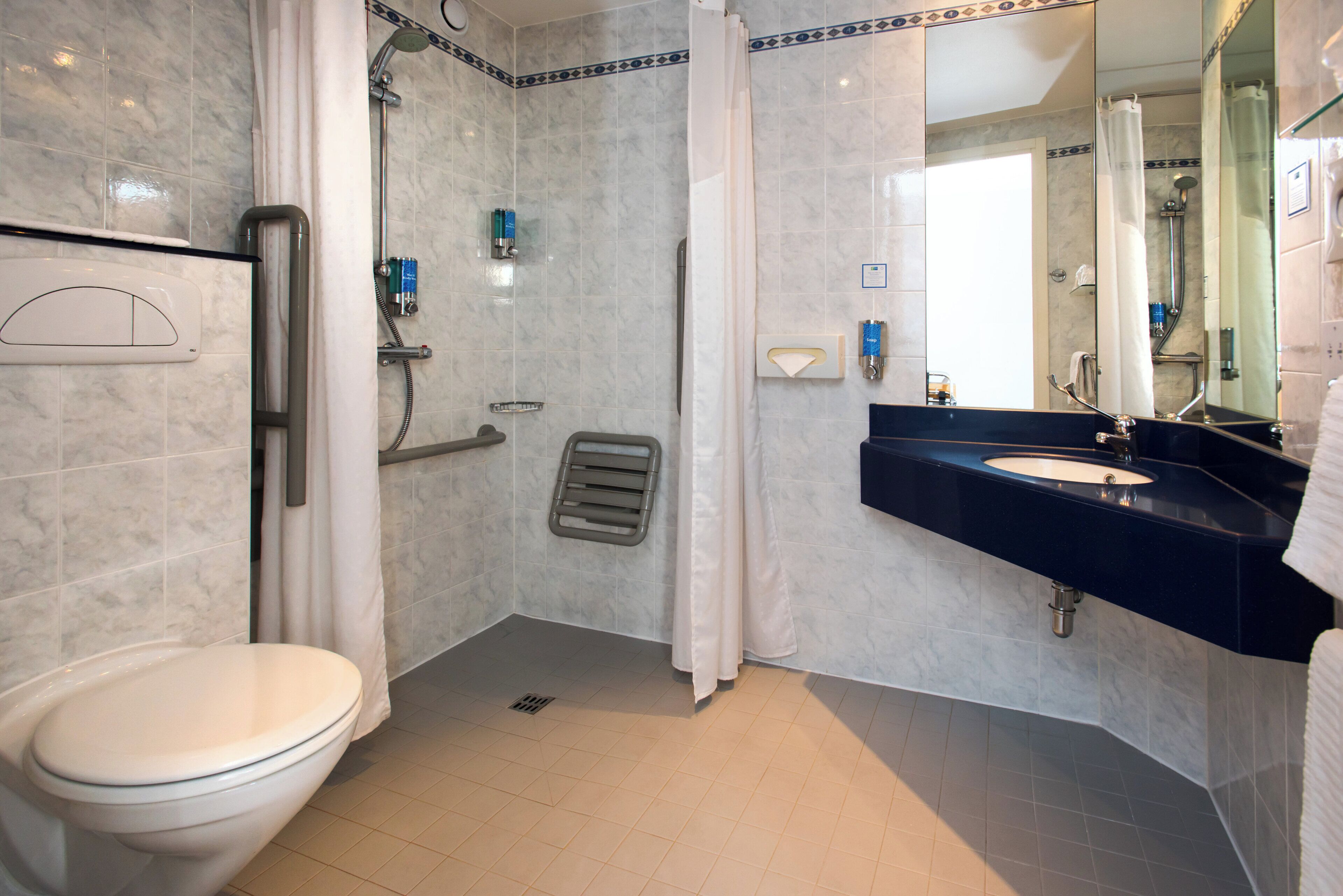 A bathroom with a toilet, a shower with a glass door, a sink with a dark countertop, and a mirror.