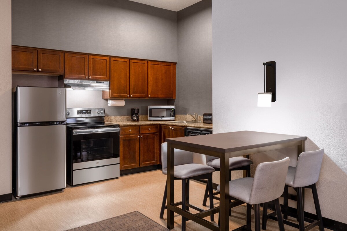 A modern kitchen with wooden cabinets, stainless steel appliances, and a dining area with a table and chairs.