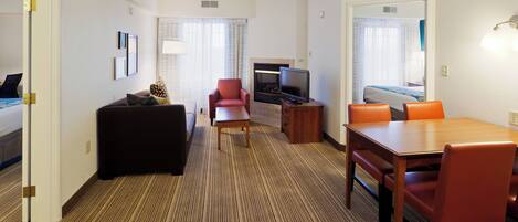 Quarto de hotel com cama, sofá, mesa de jantar com cadeiras, televisão e lareira.