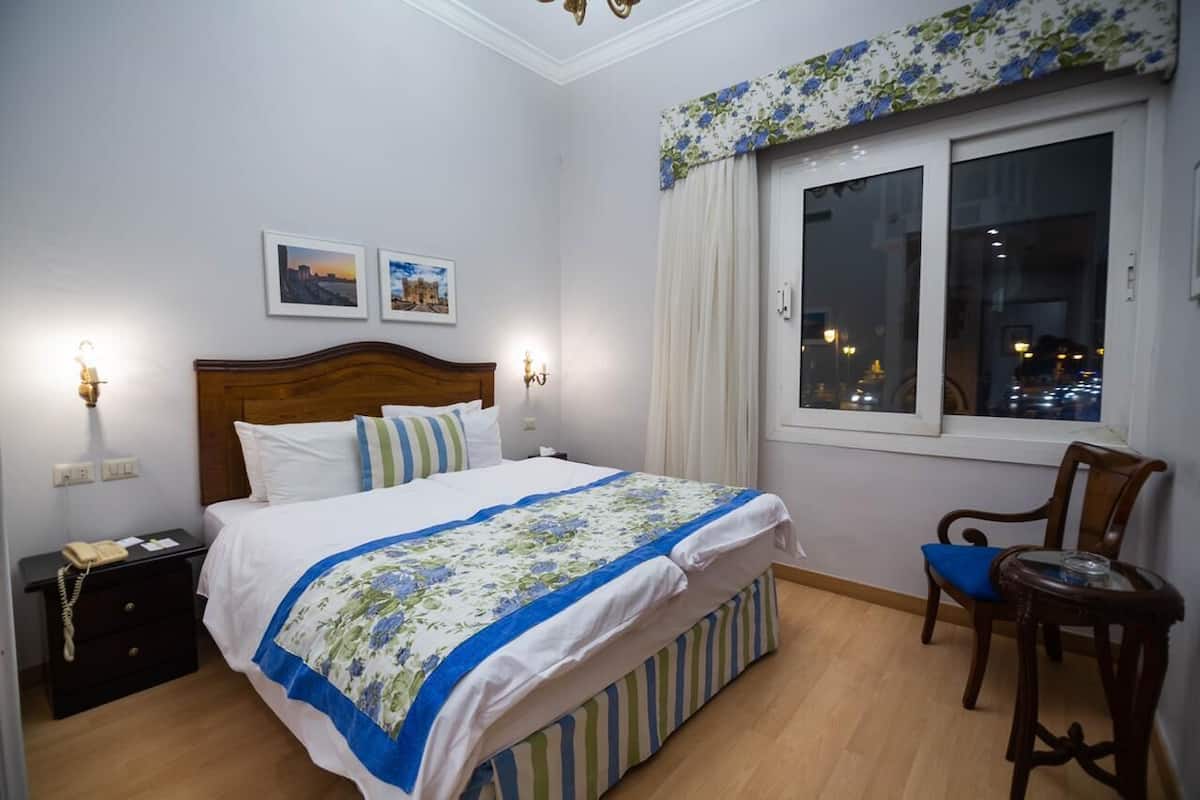 A bedroom with a wooden bed, bedside tables, a chair, and a window with curtains.
