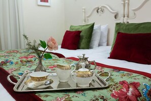 A neatly made bed with floral bedding, a tray with tea set, and a vase with a rose.