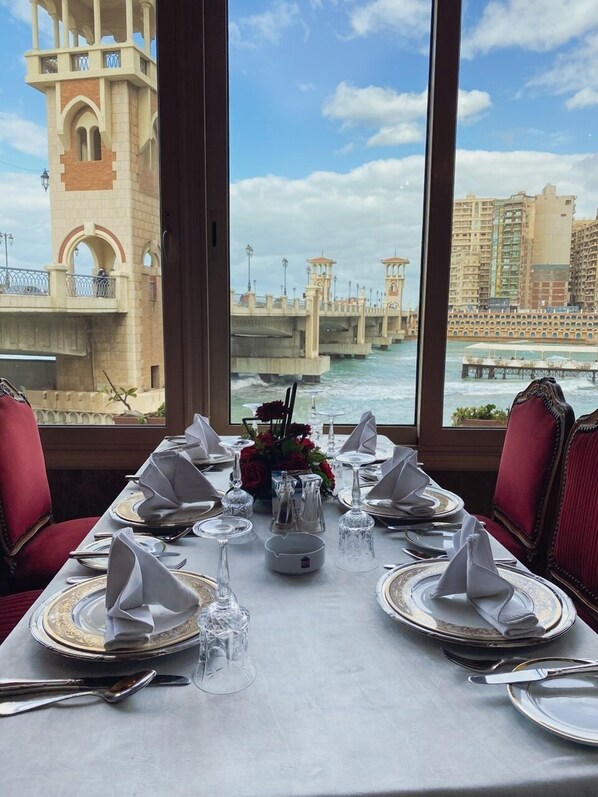 A dining table set for a meal with a view of a bridge and buildings across the water.