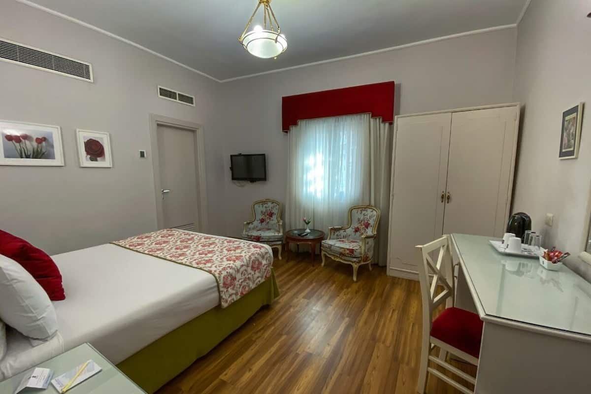 A bedroom with a bed, a desk, two chairs, a television, and a wardrobe.