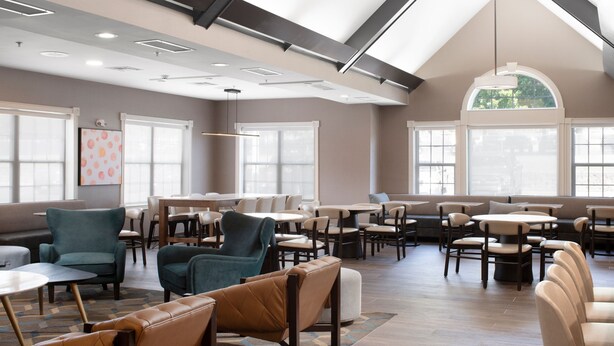 A spacious indoor area with multiple seating arrangements, including tables and chairs, and large windows providing natural light.