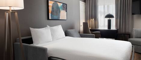 Une chambre d’hôtel avec un lit, une table de chevet, une lampe, une chaise et un tableau au mur.