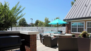 An outdoor patio with a grill, wicker furniture, and a pool area.