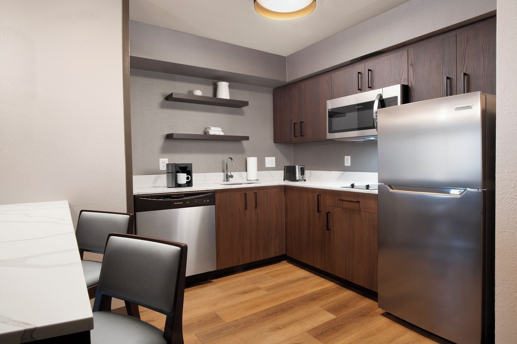 A modern kitchen with wooden cabinets, a stainless steel refrigerator, a microwave, and a dishwasher.