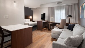 A modern hotel room with a wooden desk, a sofa, a bed, and a TV.