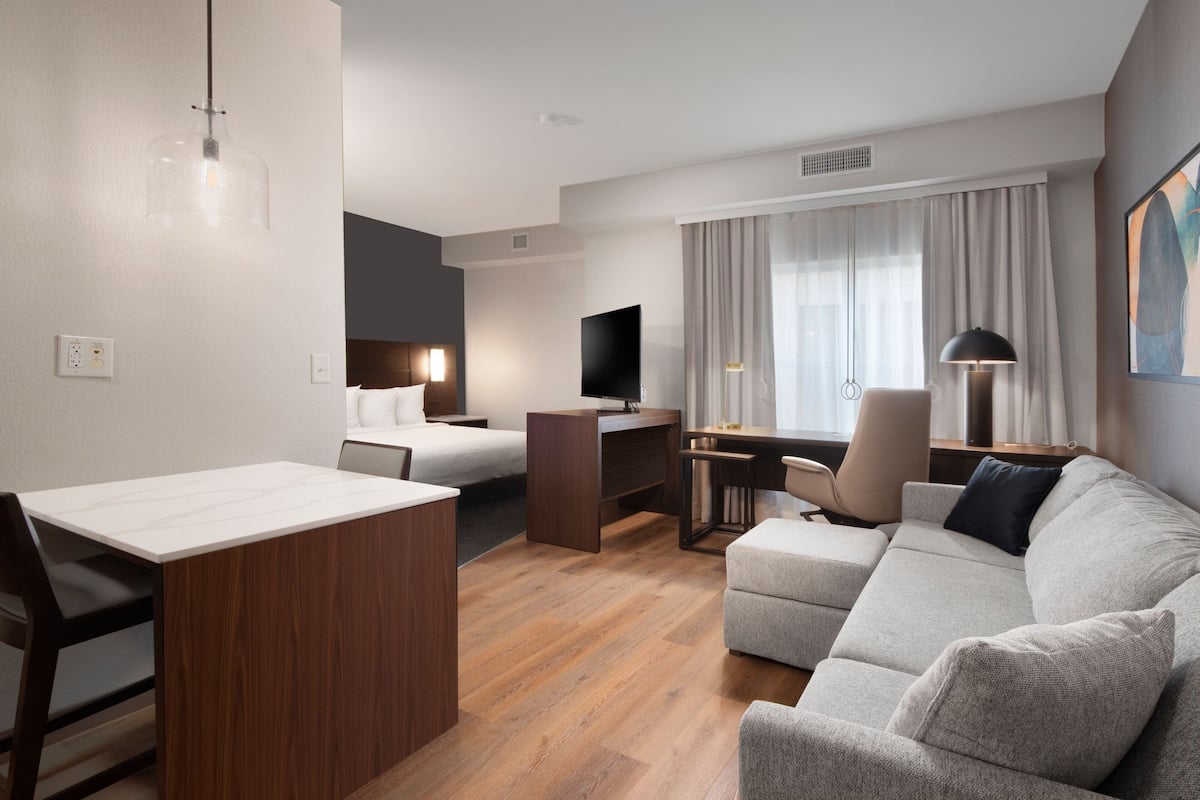 Una habitación de hotel moderna con un escritorio de madera, un sofá, una cama y un televisor.