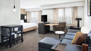 Quarto de hotel com cama, escrivaninha, duas cadeiras, um sofá e televisão.