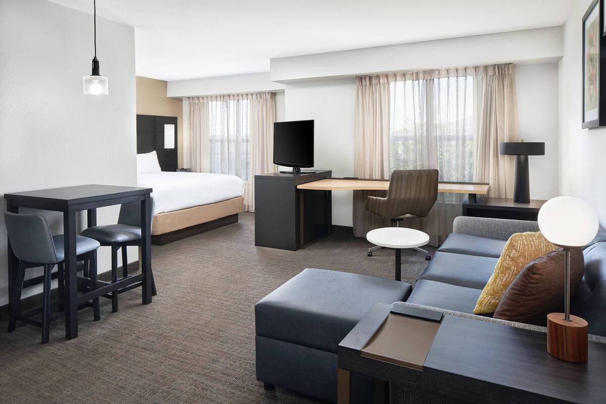 A hotel room with a bed, desk, two chairs, a sofa, and a TV.