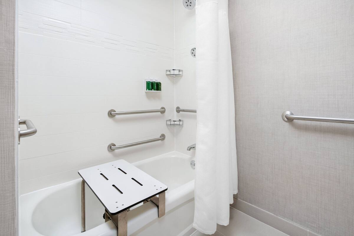 A modern bathroom with a bathtub, grab bars, and a shower curtain.