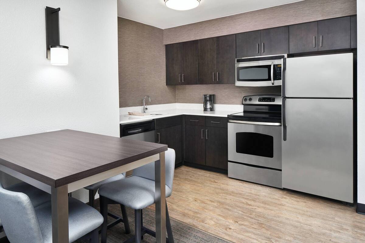 A modern kitchen with dark cabinets, stainless steel appliances, a wooden table, and two chairs.