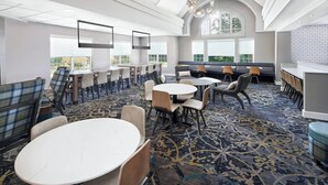Um espaço de refeições moderno em hotel, com mesas redondas, assentos confortáveis e grandes janelas com vista.