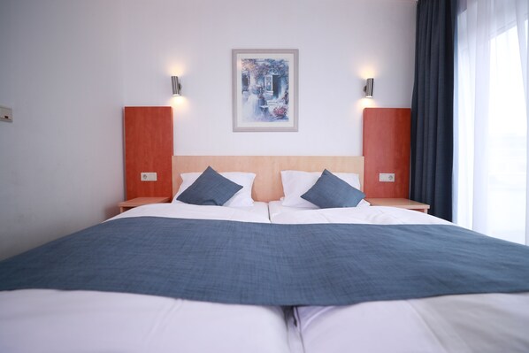 A hotel room with a large bed, two nightstands, a framed picture on the wall, and a window with curtains.
