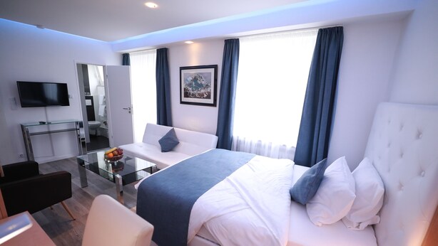 A modern hotel room with a large bed, a desk, a flat-screen TV, and a glass coffee table. - Hotel Savoy Bonn (Bonn)