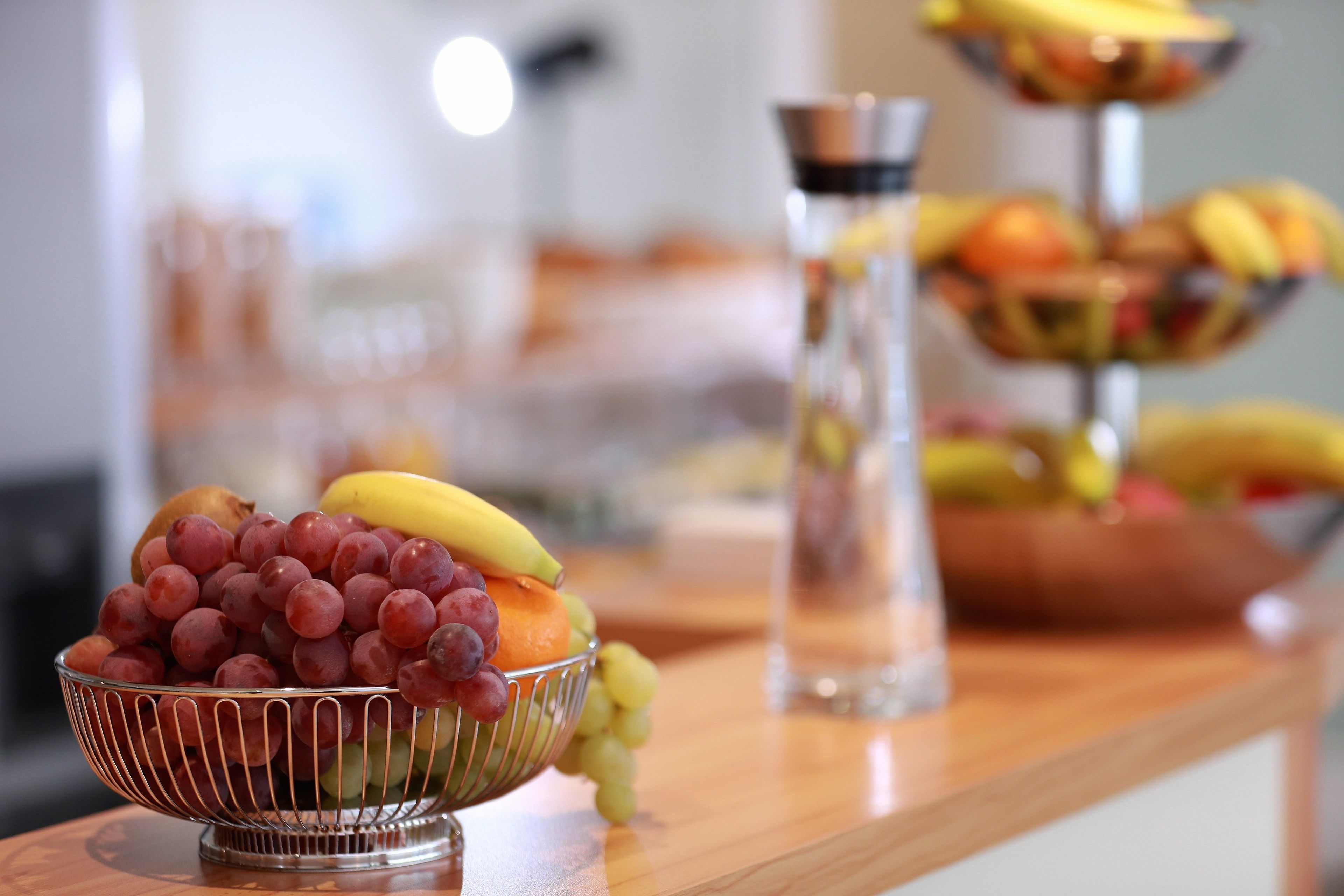 A fruit bowl with grapes, bananas, and oranges on a wooden counter.