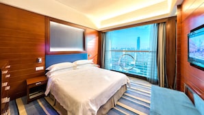 Habitación de hotel con una cama grande, televisión, ventana con vista a la ciudad y pared de paneles de madera.