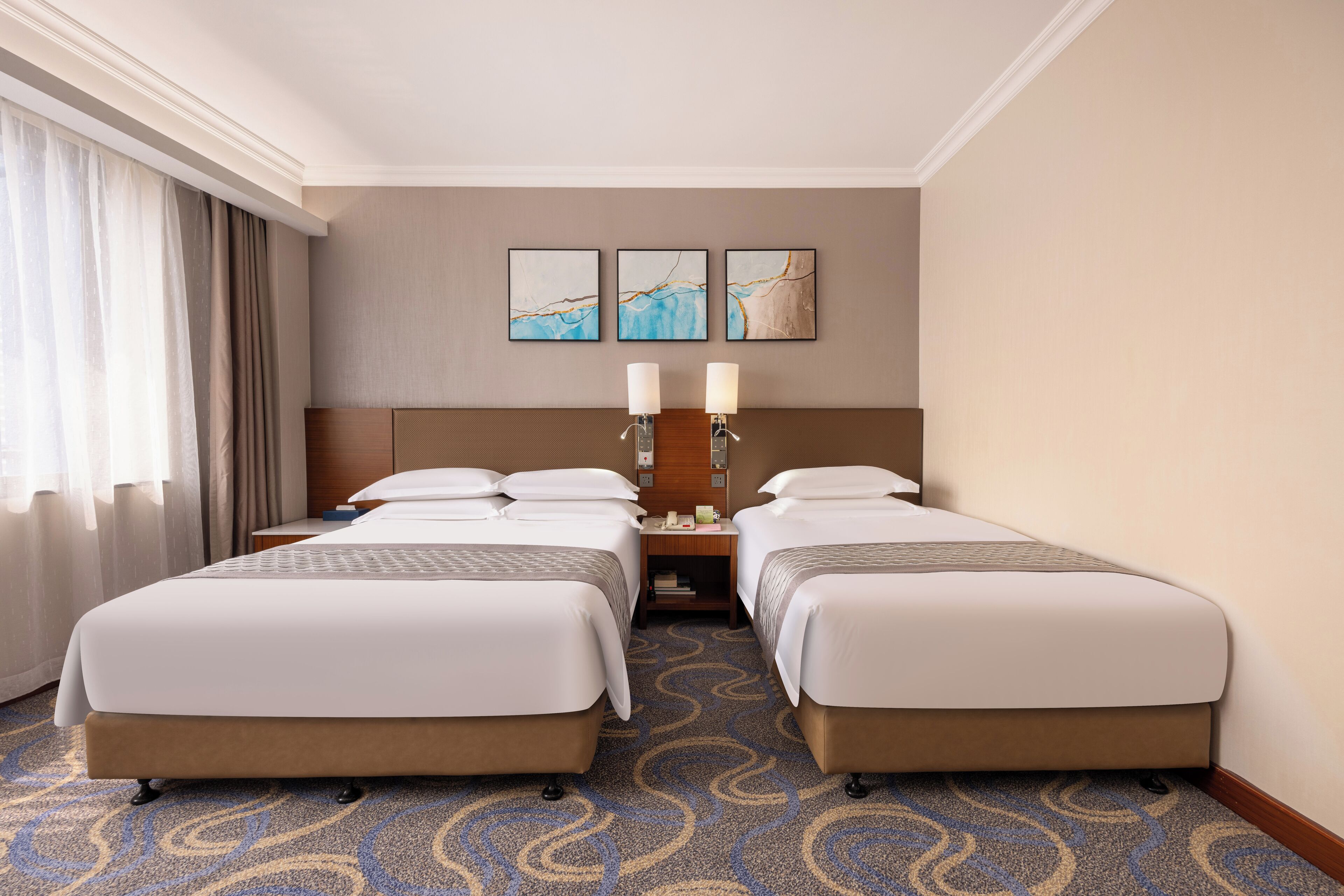 A hotel room with two beds, a nightstand with candles, and three abstract wall art pieces.