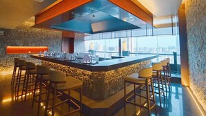 Zona de bar moderna con una barra central, taburetes y vistas a la ciudad a través de amplios ventanales.