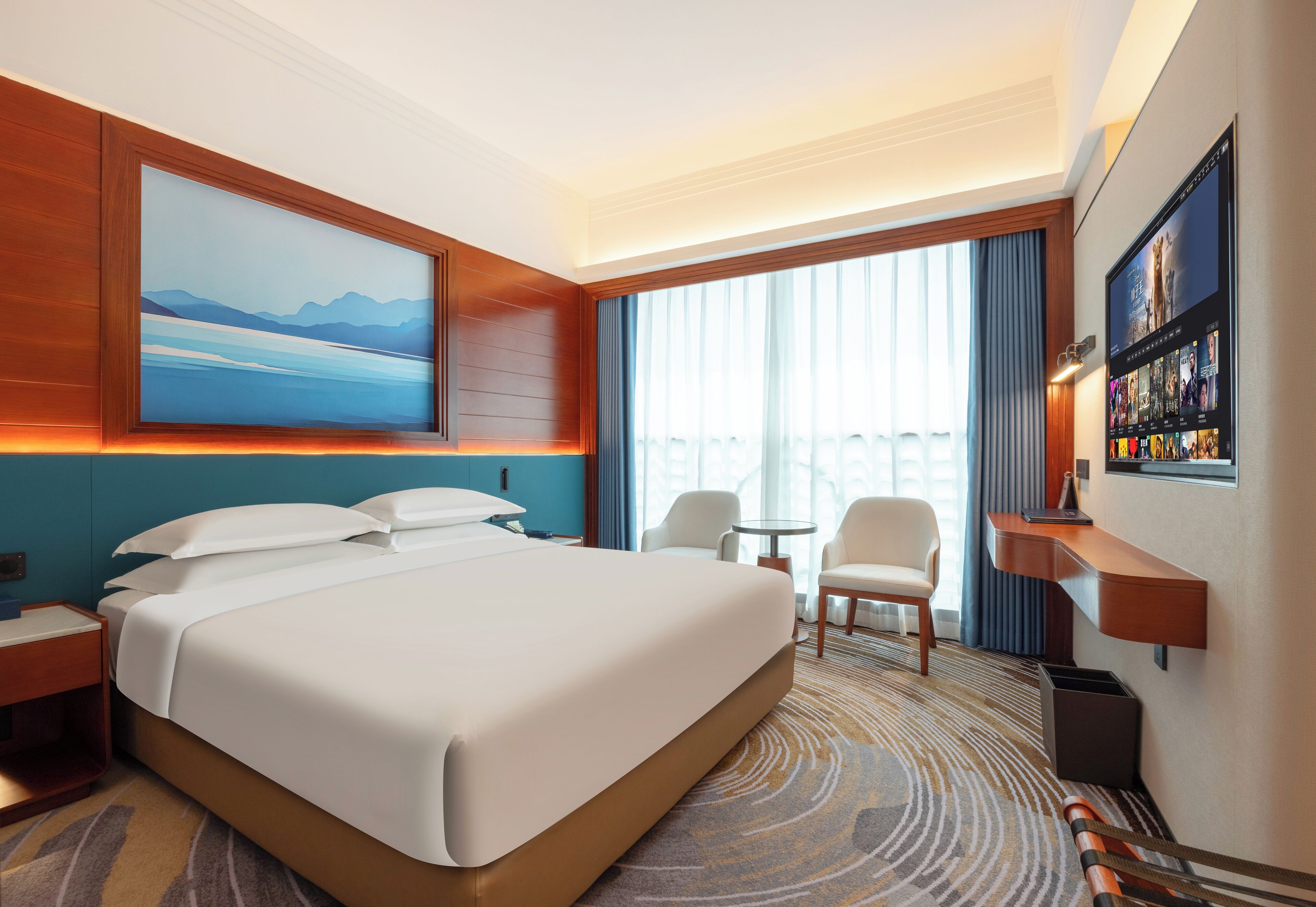 A hotel room with a large bed, a desk, a chair, a small table, and a TV on the wall.