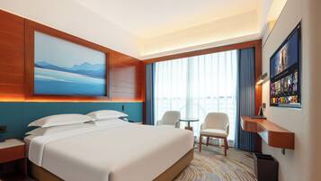 A hotel room with a large bed, a desk, a chair, a small table, and a TV on the wall.