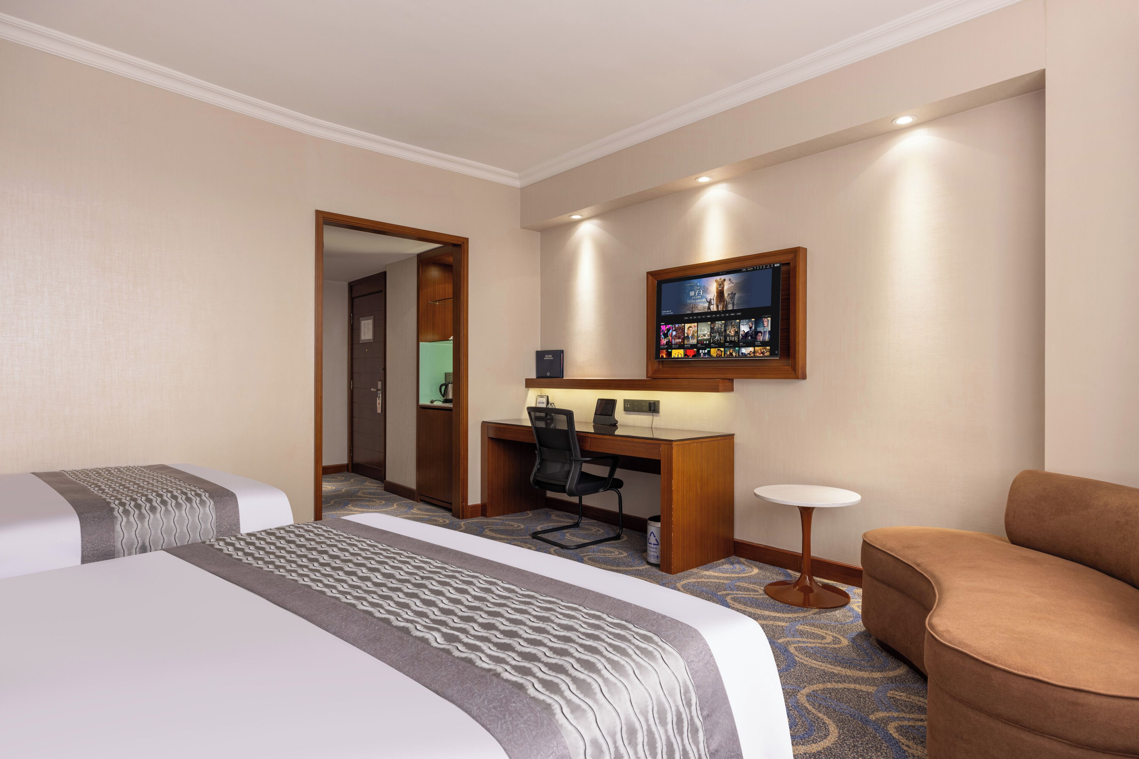 A hotel room with two beds, a desk with a computer, a TV mounted on the wall, and a small round table.