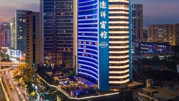 Un hotel de varios pisos con un letrero vertical llamativo, una fachada curva y un área en la azotea con luces.