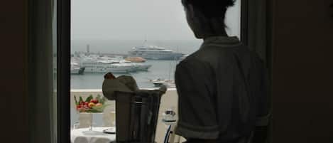 A room with a view of a port, a table with a fruit bowl, and a metal container.
