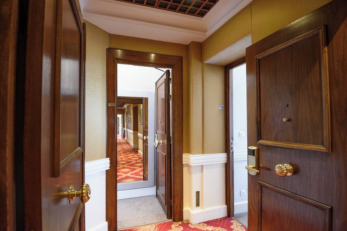 A hallway with wooden doors, a red carpet, and a view into another room.