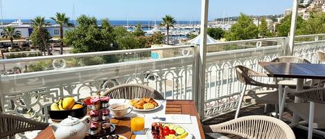 Een balkon met een ontbijttafel, compleet met fruit, gebak en een theepot.