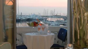A table with a bottle, glasses, and a vase of branches, overlooking a marina with boats. - Hotel Splendid Cannes (Cannes)