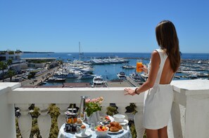 A balcony with a table set for breakfast overlooking a marina with boats. - Hotel Splendid Cannes (Cannes)