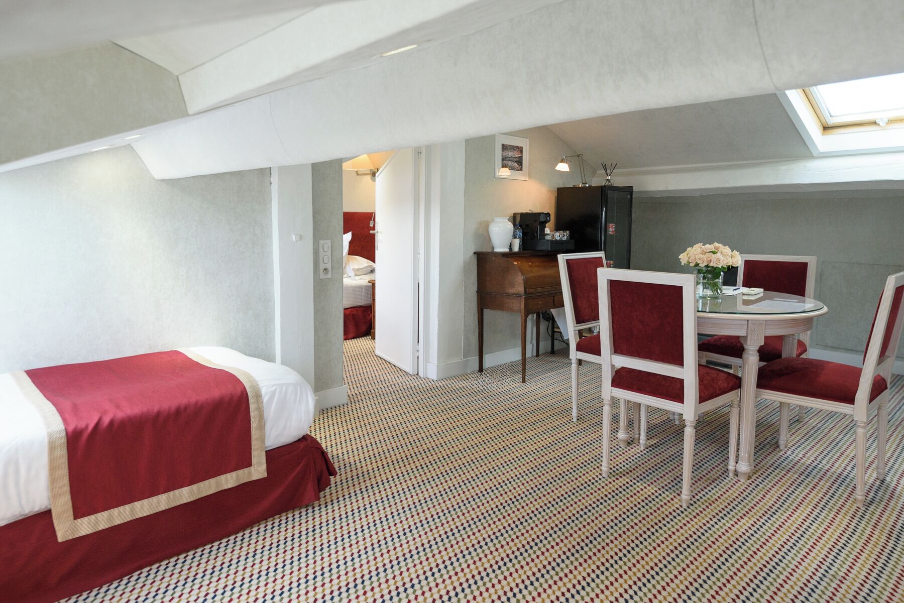 A hotel room with a bed, a small dining table with chairs, a kitchenette, and a view through an open door.