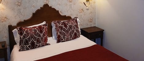 A hotel room with a bed, floral wallpaper, a framed picture on the wall, and a nightstand.