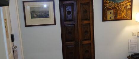 Habitación de hotel con una cama, una puerta de madera, un cuadro enmarcado y una lámpara fijada a la pared.
