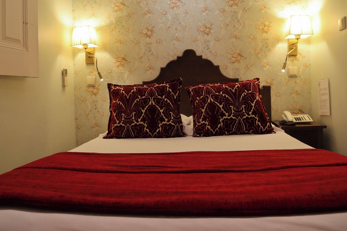 Habitación de hotel con cama, dos lámparas de pared, teléfono y papel tapiz floral.