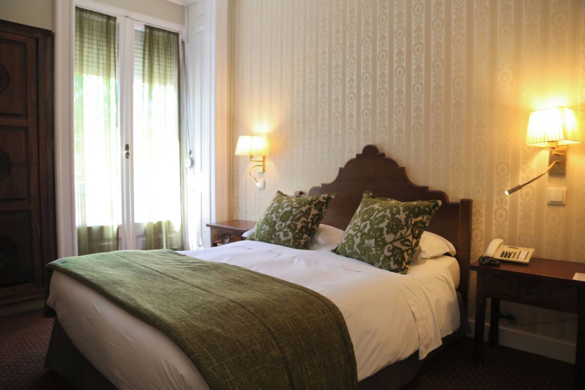 Una habitación de hotel con una cama grande, dos lámparas de noche, una mesita de noche y un teléfono.