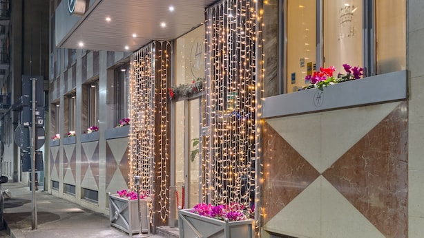 A hotel entrance with a neon sign, decorative lights, and flower arrangements.