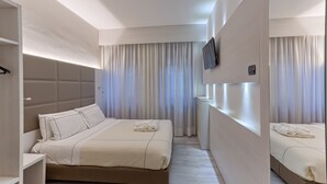 A modern hotel room with a large bed, a bedside table, a TV mounted on the wall, and a large mirror.