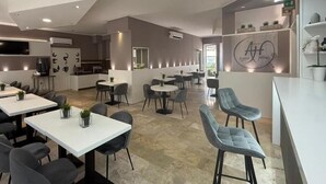 A modern hotel lobby with a bar area, seating arrangements, and a visible kitchen in the background.