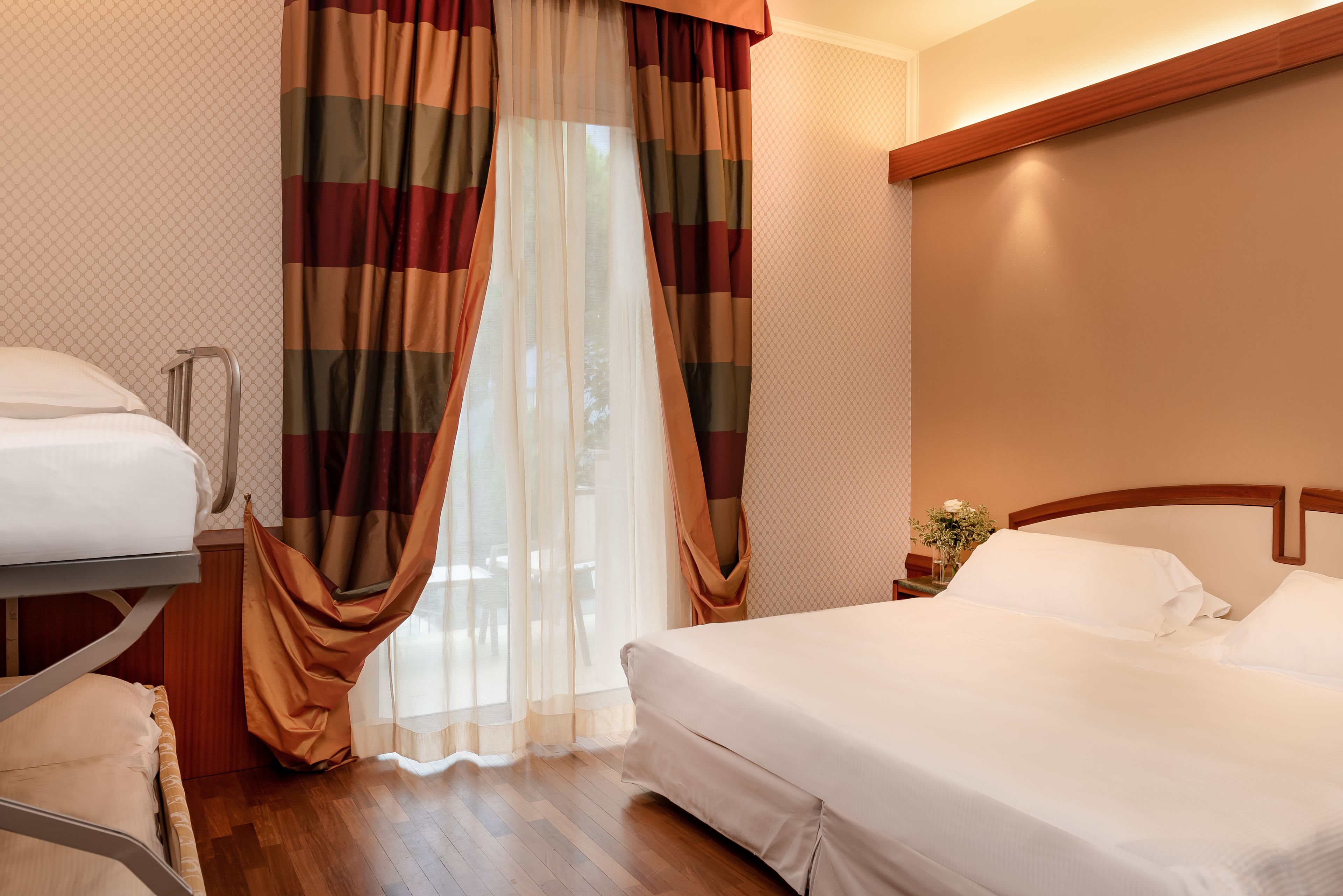 A hotel room with a bed, a bedside table, and a window with curtains.