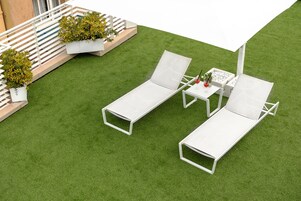 Due poltrone bianche con un tavolino e un ombrellone bianco su un prato sintetico verde.