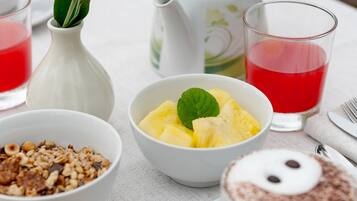 Una mesa con alimentos para el desayuno, incluyendo un tazón de trozos de piña, un pastel y una taza de café.