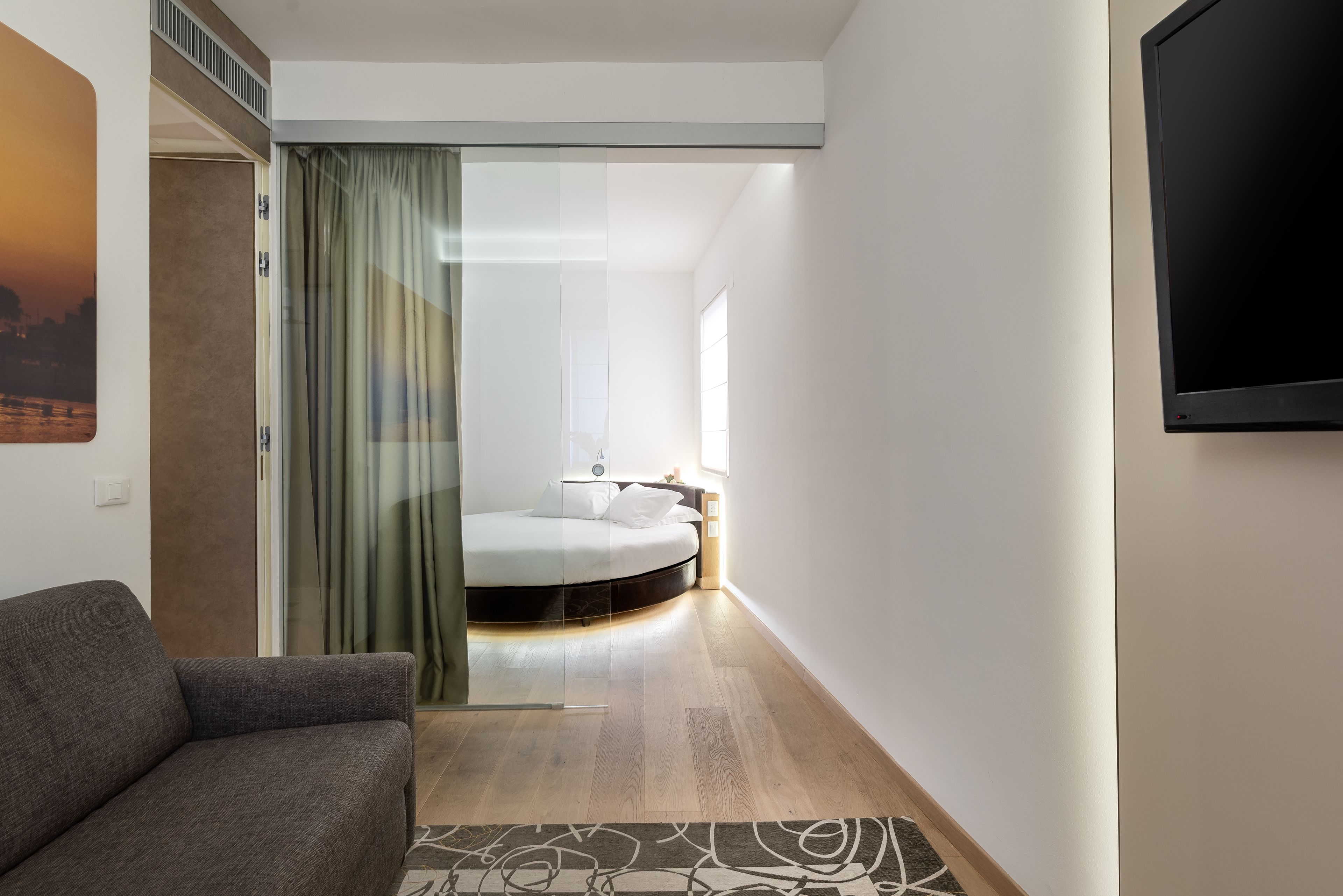 Una camera d'albergo moderna con un divano, un letto, una TV e una porta vetrata che dà su un balcone.