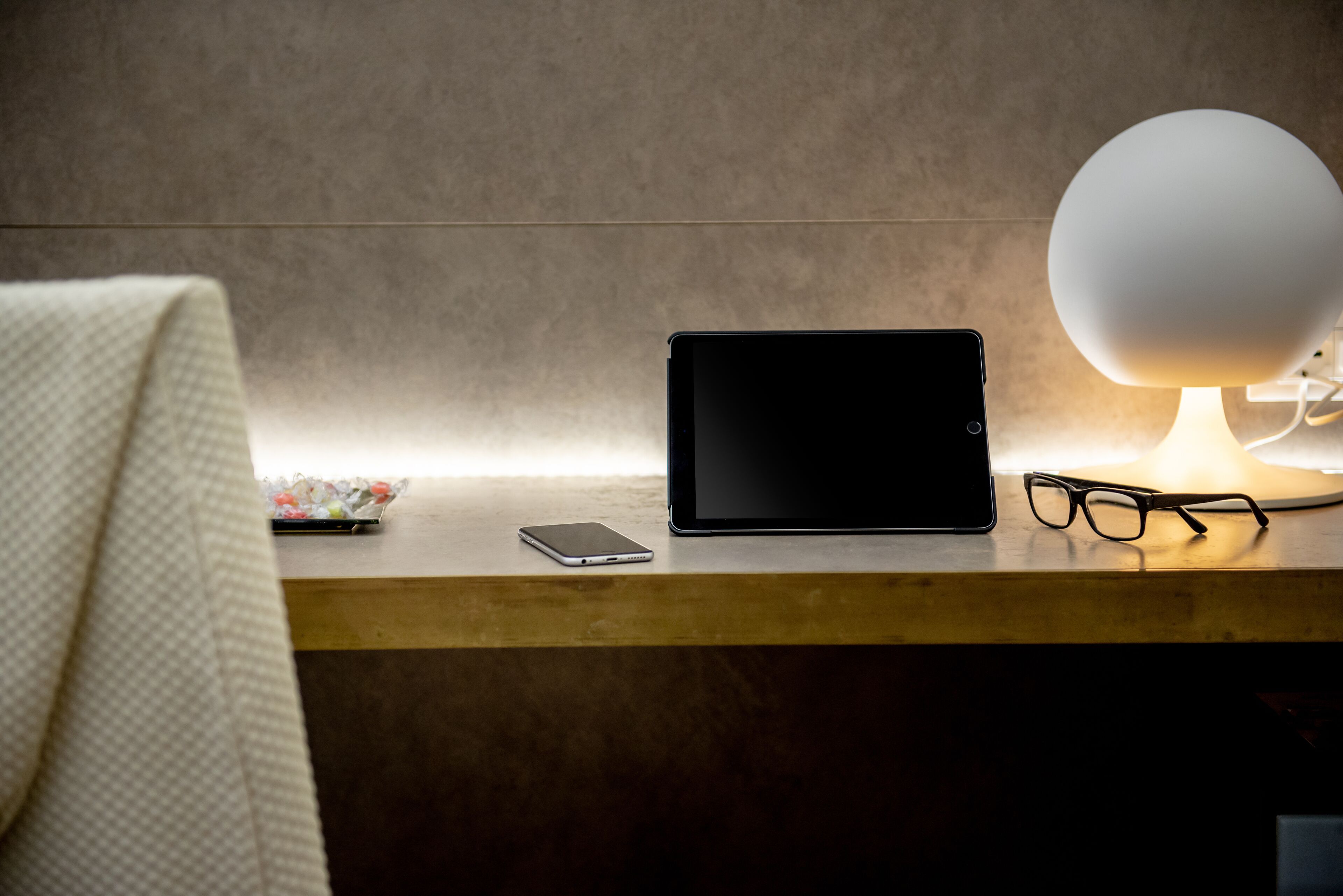 A wooden desk with a tablet, smartphone, and a pair of glasses.