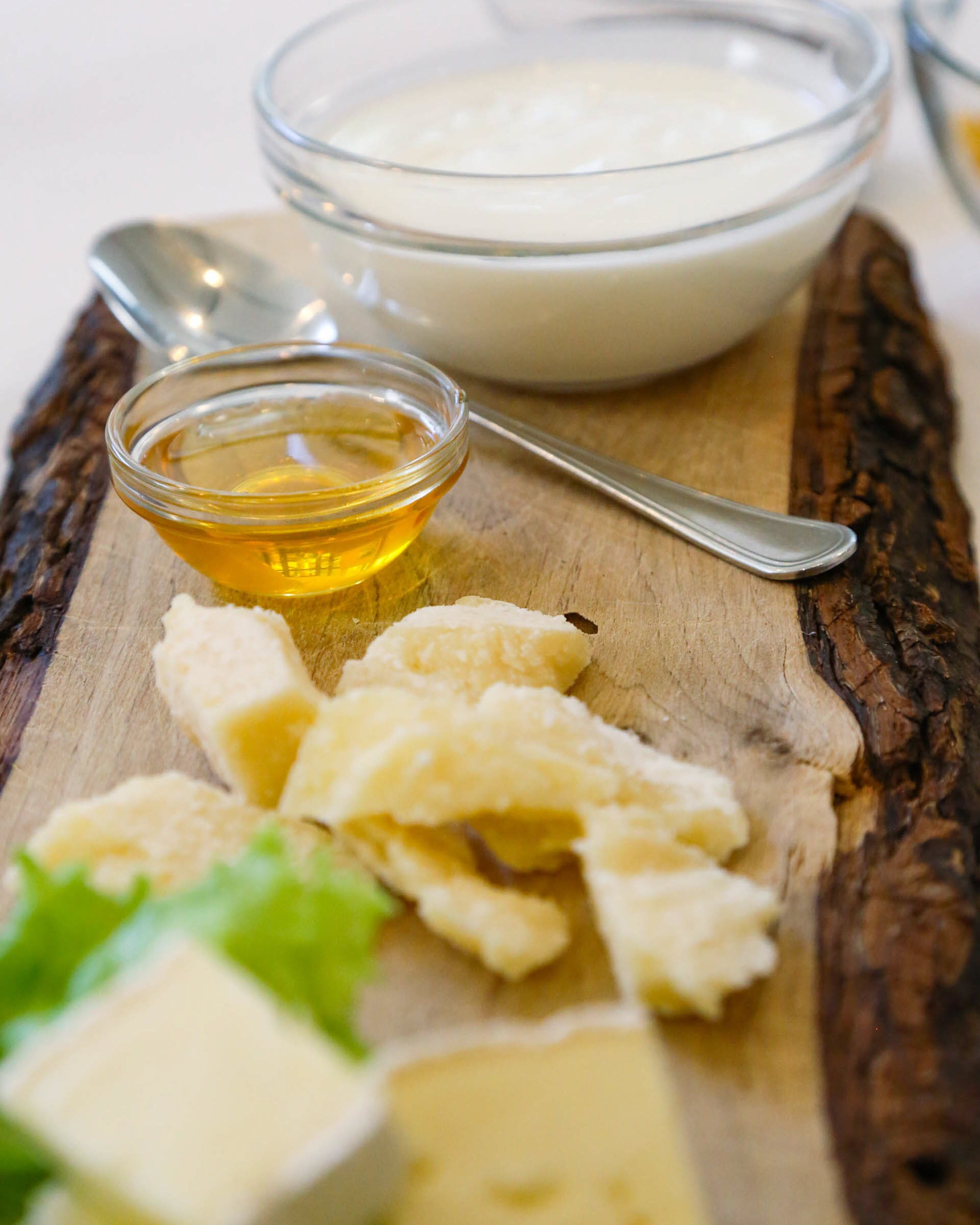 A wooden board with cheese, a bowl of dip, and a small bowl of honey.