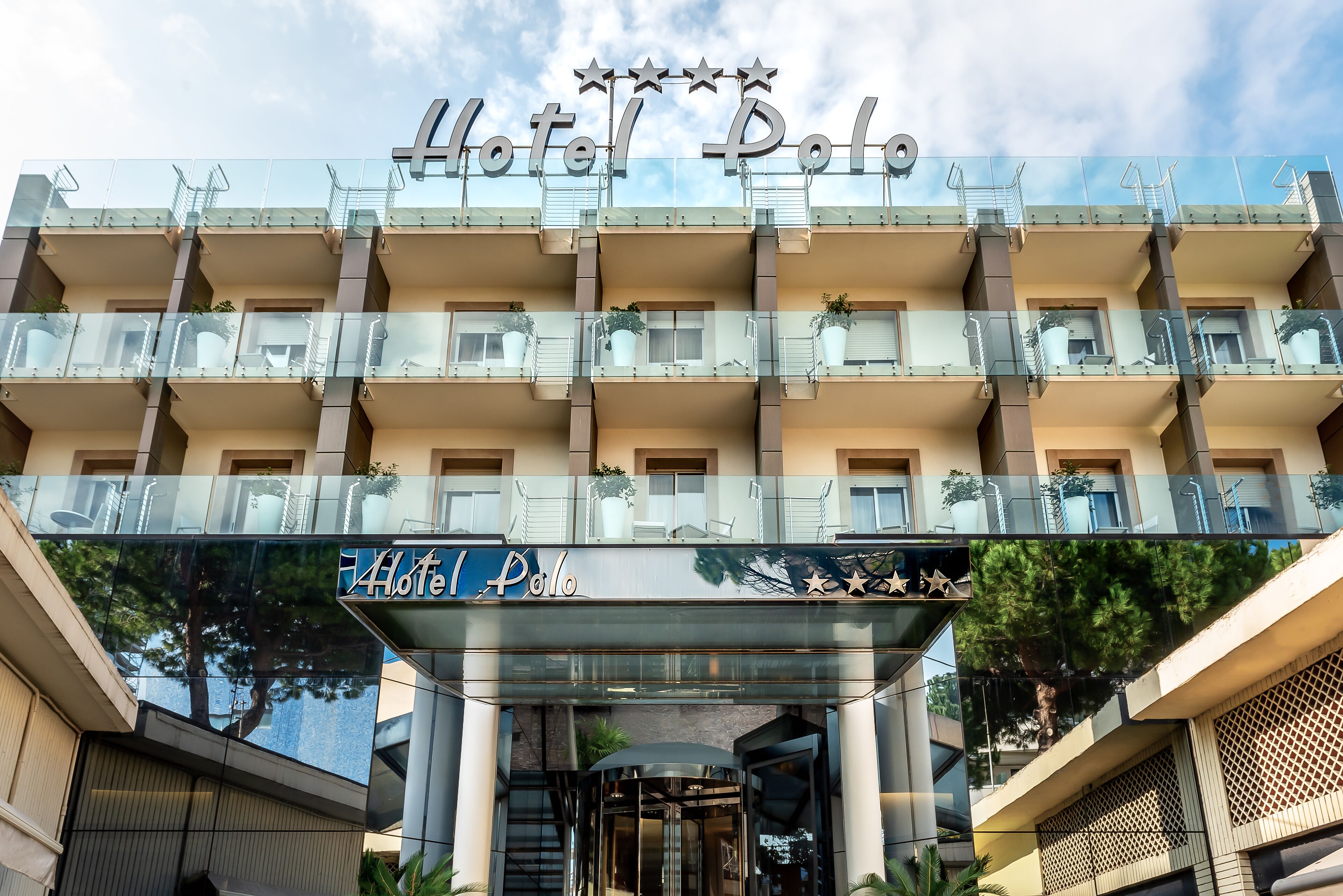 A multi-story hotel with a glass facade, balconies with railings, and a sign reading "Hotel Polo".