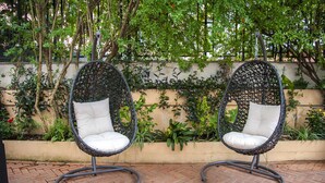Two wicker chairs with white cushions, positioned on a brick patio with a garden wall and greenery in the background. - Hotel Delle Province (Rome)